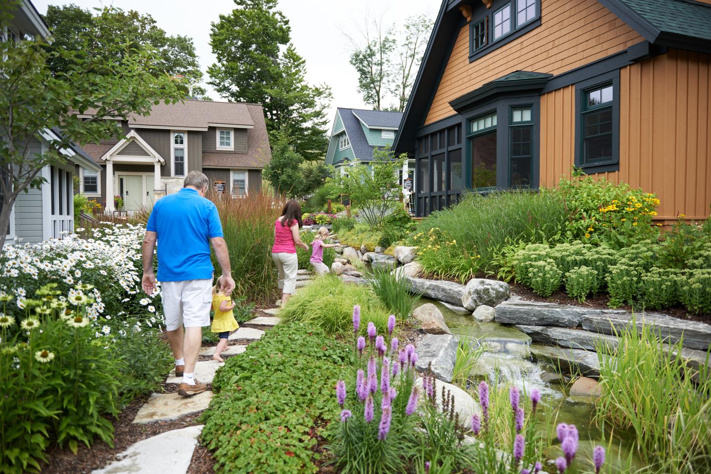 Family walking along a garden path with flowers and modern houses.