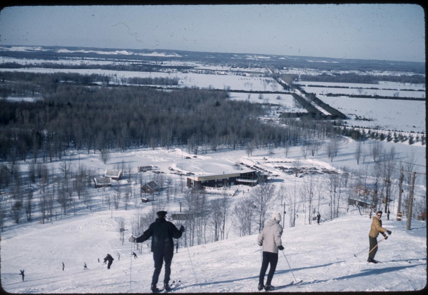 Skiers descend a snowy hill with a distant view of Thompsonville.