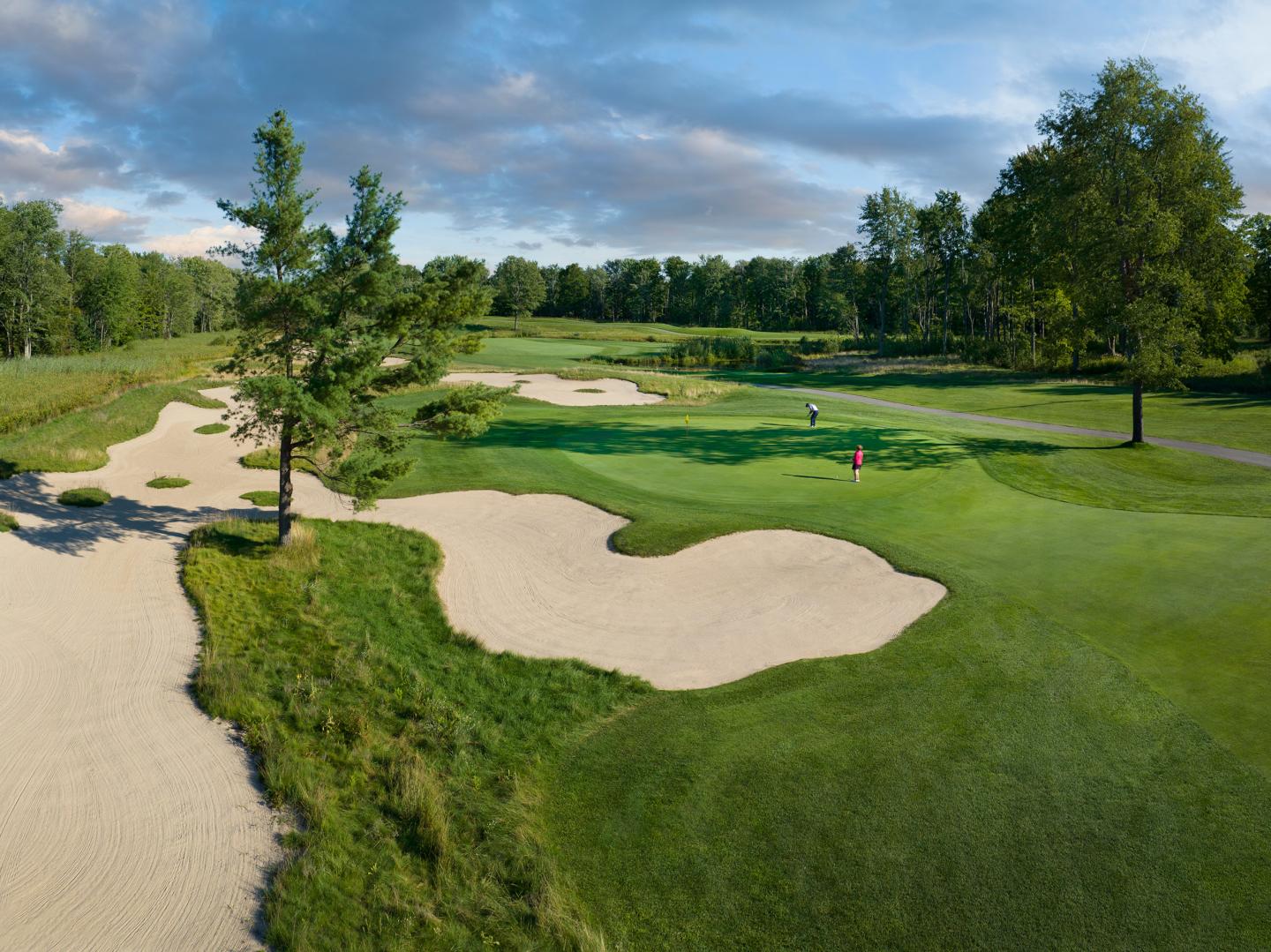 Golf course with sand traps, green grass, and trees under a cloudy sky.