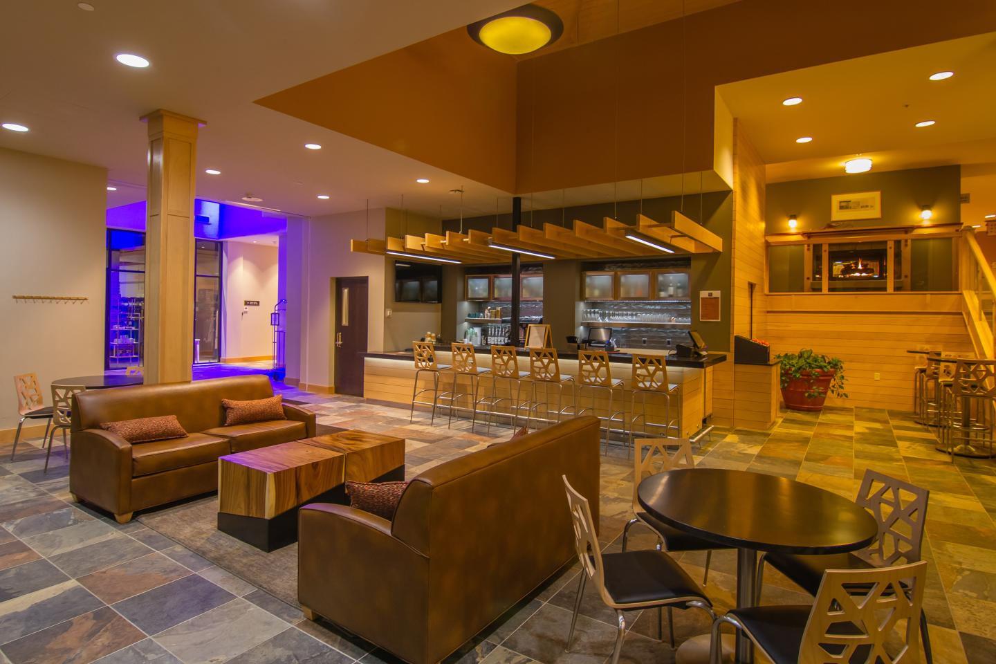 Lobby with brown couches, tables, bar, and blue accent lighting.
