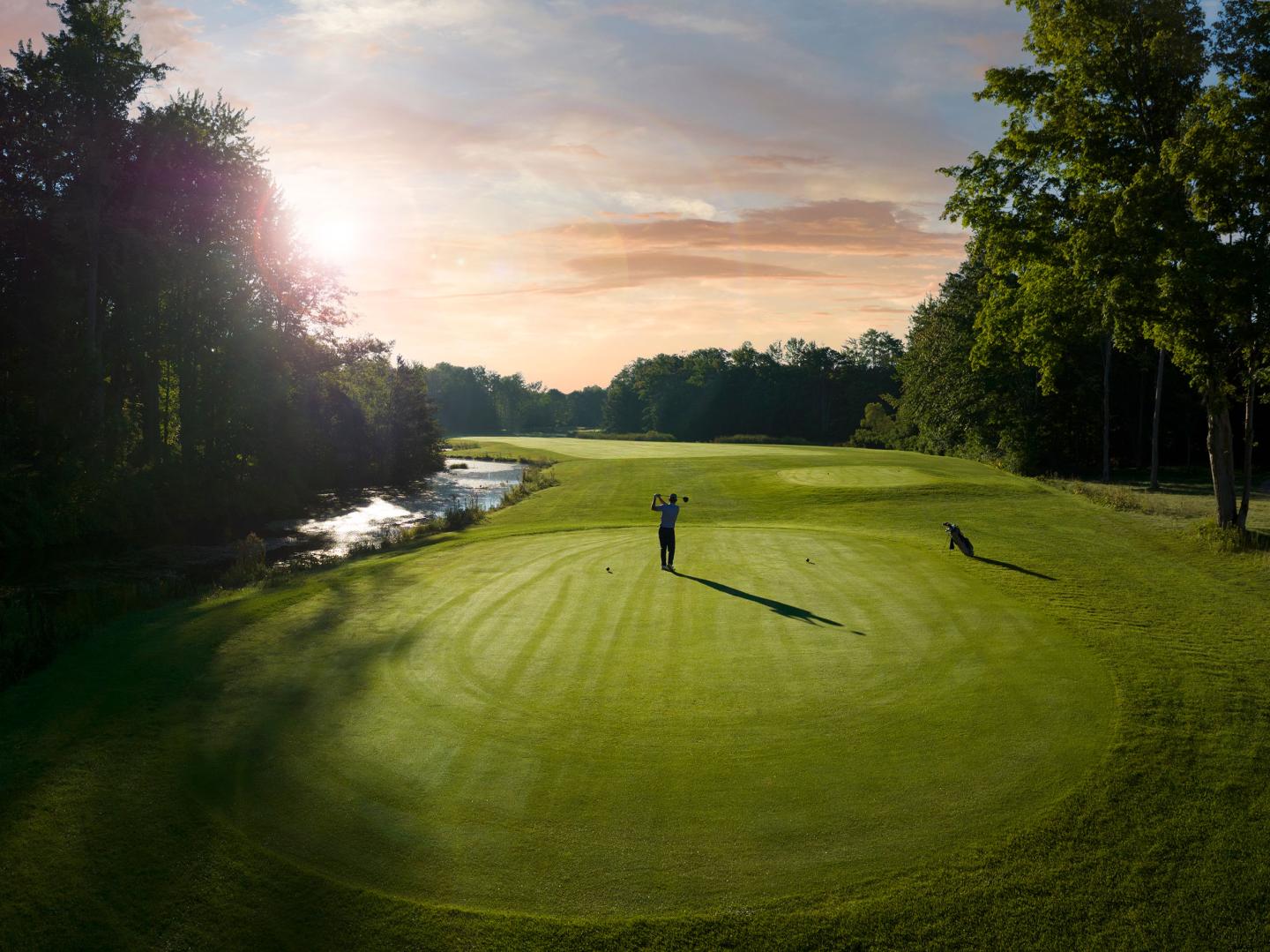 Golf course at sunset with player on the green, shadow cast long.