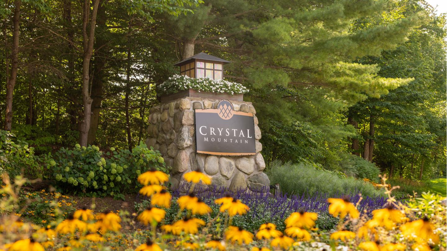 Stone entrance sign with flowers and lush greenery.