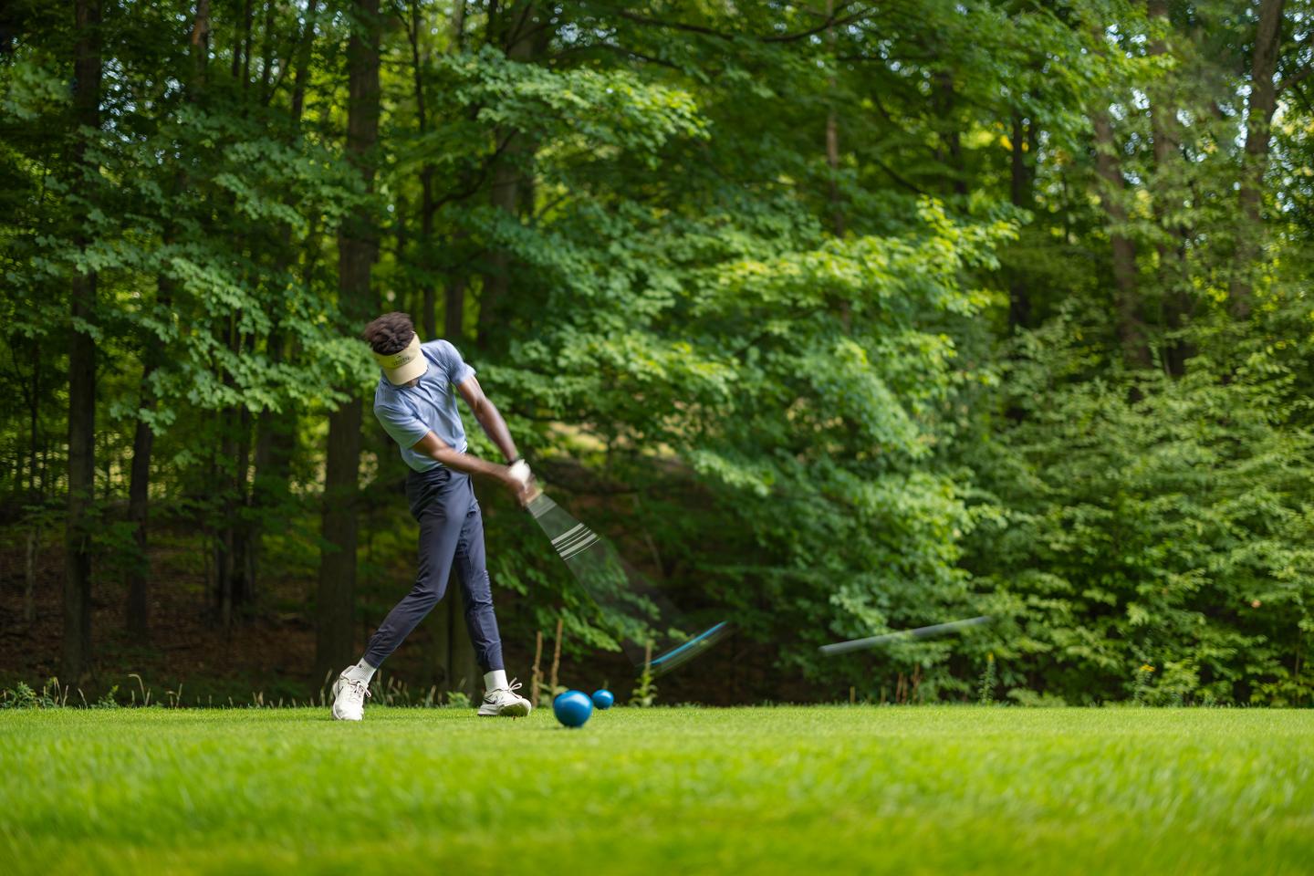 Golfer swinging club on lush green course surrounded by trees.