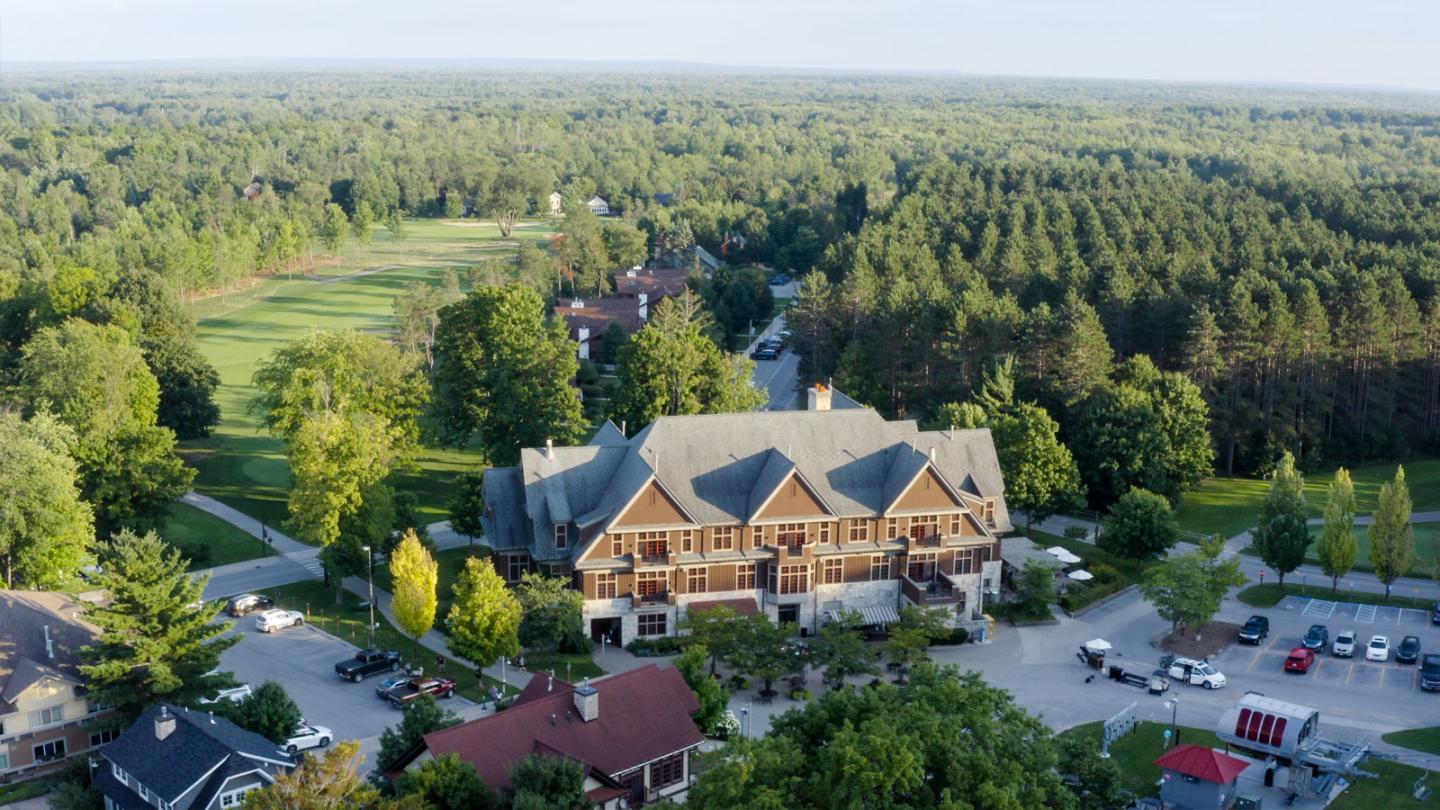 Lodge surrounded by trees, with a golf course in the background.