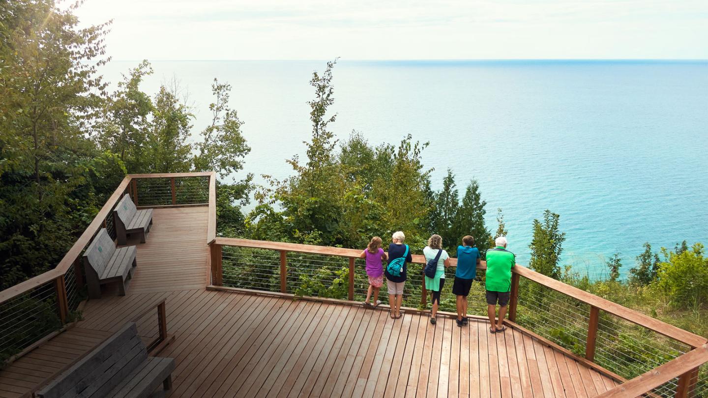 Group overlooking a scenic lake from a wooden deck surrounded by trees.