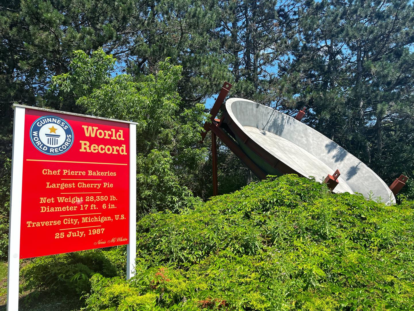 Large cherry pie sculpture next to a red world record sign, surrounded by green foliage.