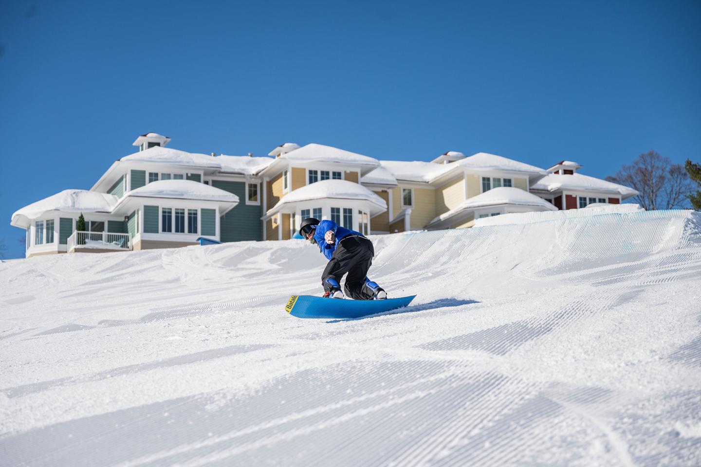 Snowboarder on snowy mountain near MountainTop townhomes and clear blue sky.