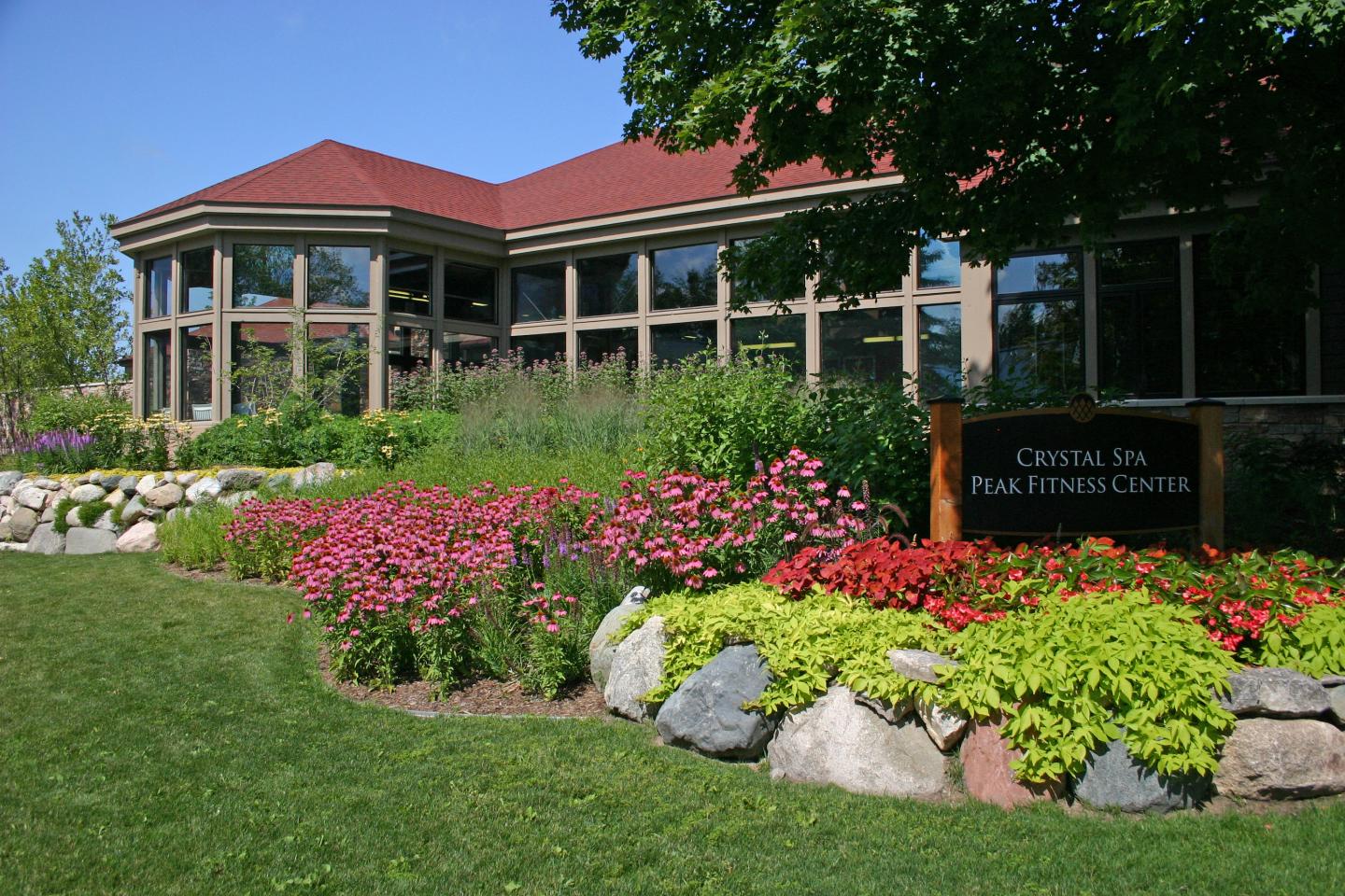 A building with large windows, surrounded by colorful flower beds and a grassy lawn.