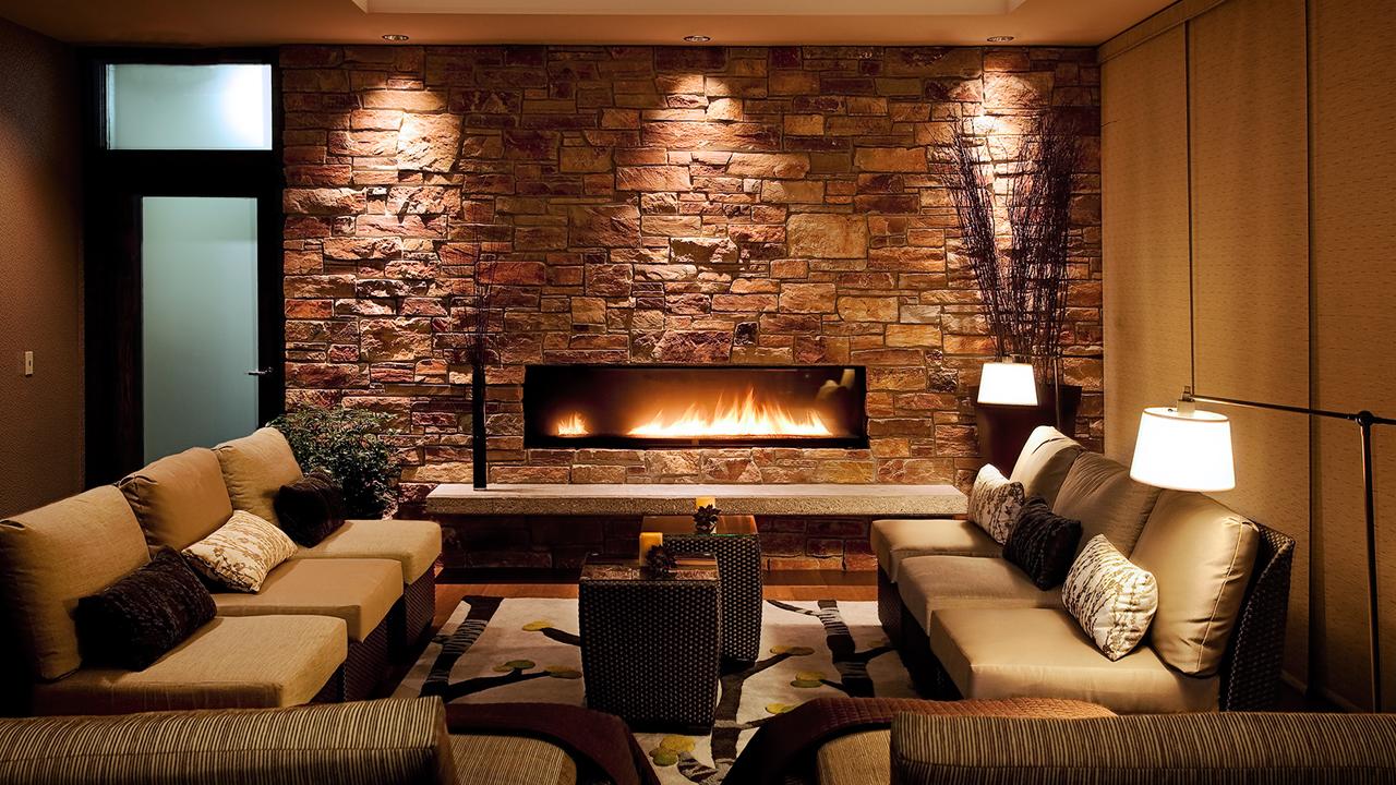 Modern living room with cozy sofas, brick wall, and a lit horizontal fireplace.