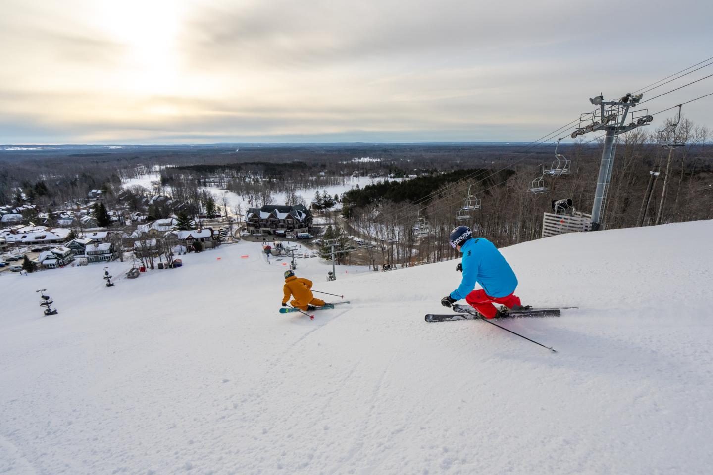 Skiers on a snowy slope with a distant view of Kinlochen and trees.