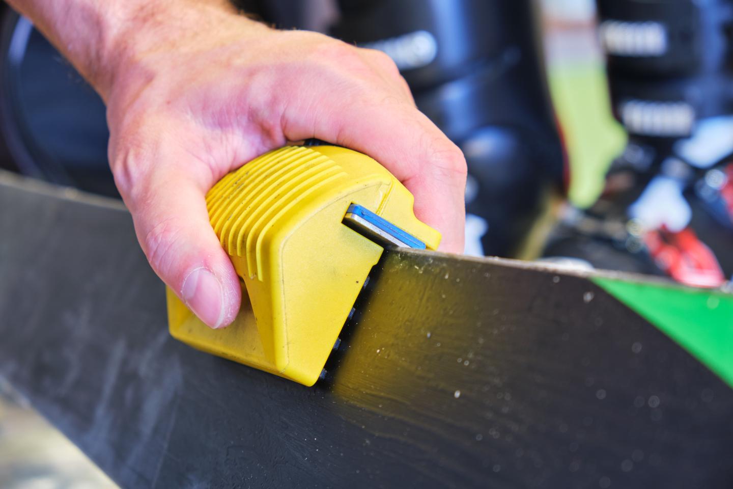 Hand sharpening a ski edge with a yellow tool.