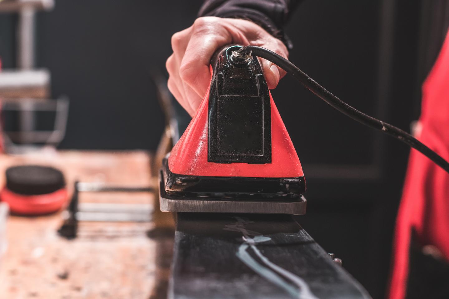 Waxing a ski with a red iron on a workbench.