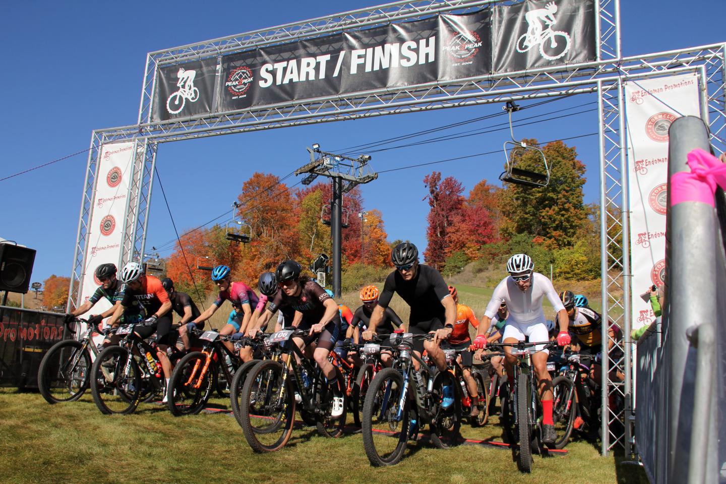 Cyclists at a race start line with autumn trees behind.