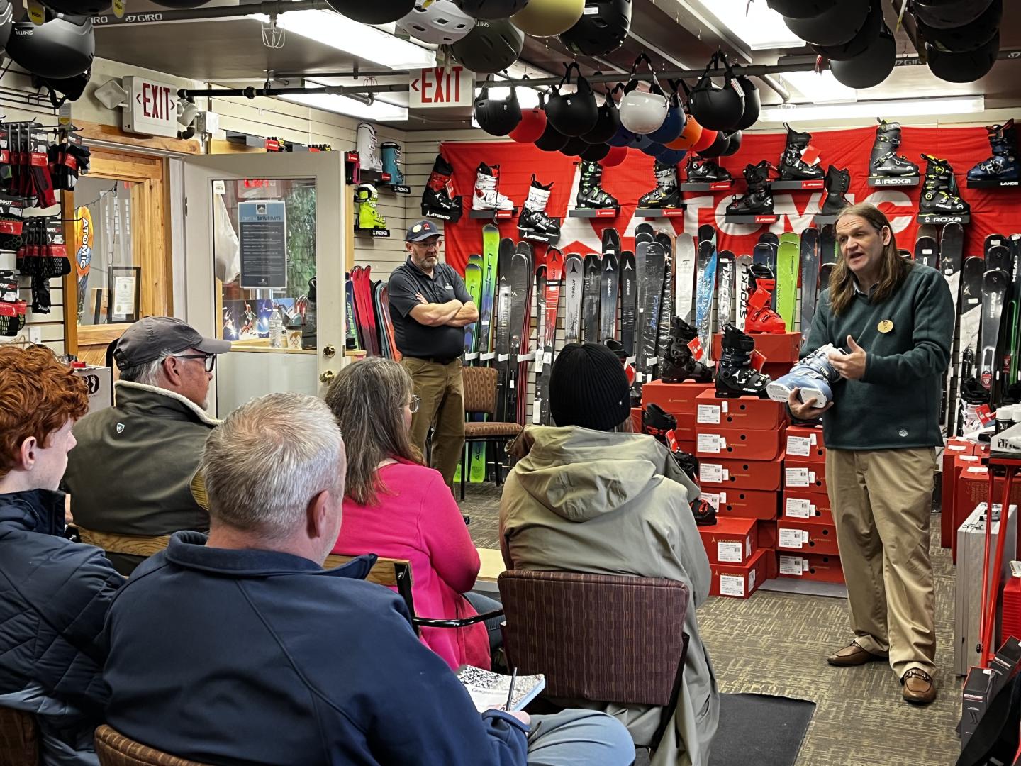 Ski shop with guide and seated students, boots in the background.