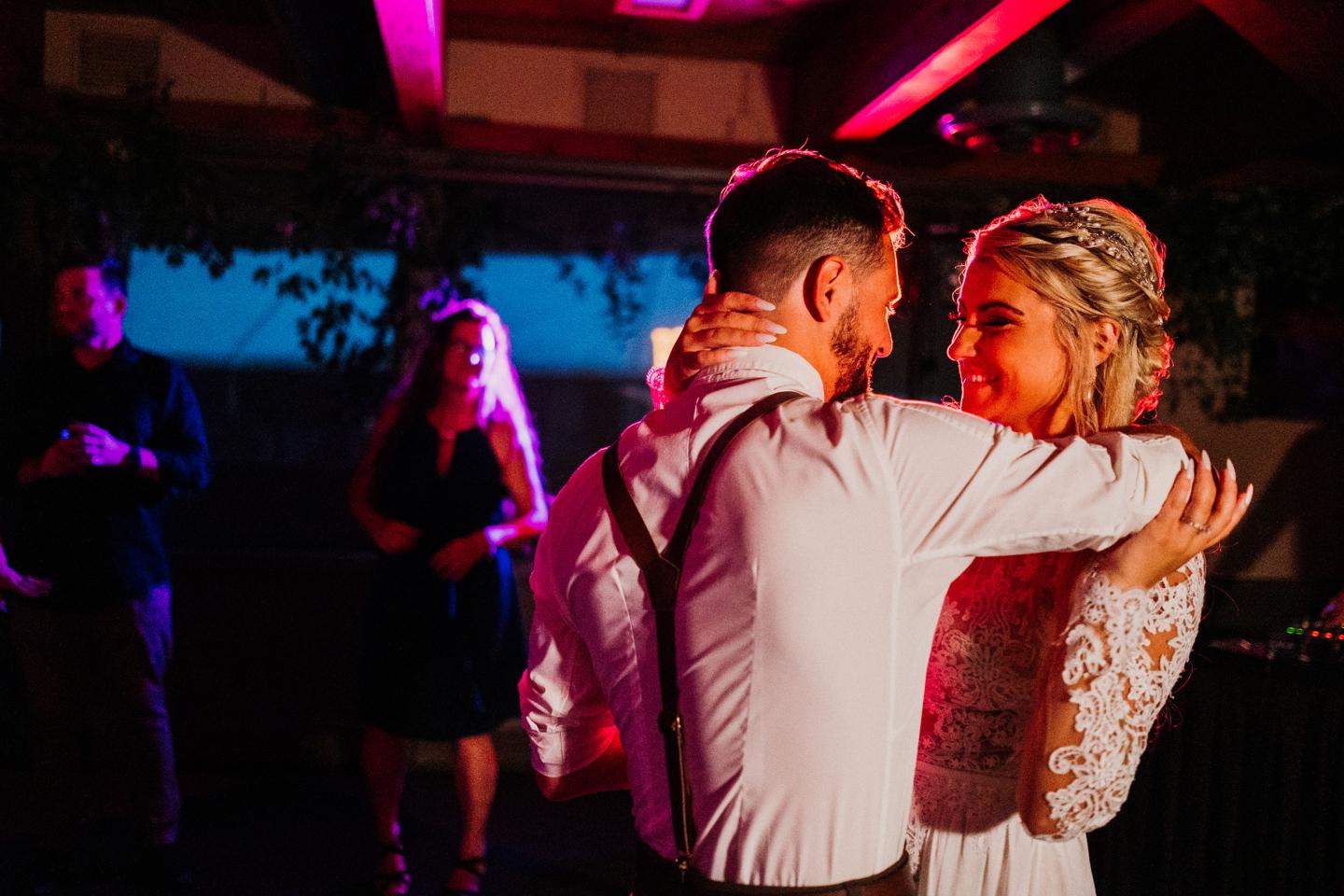 A couple dances closely under warm, colorful lighting at their wedding.