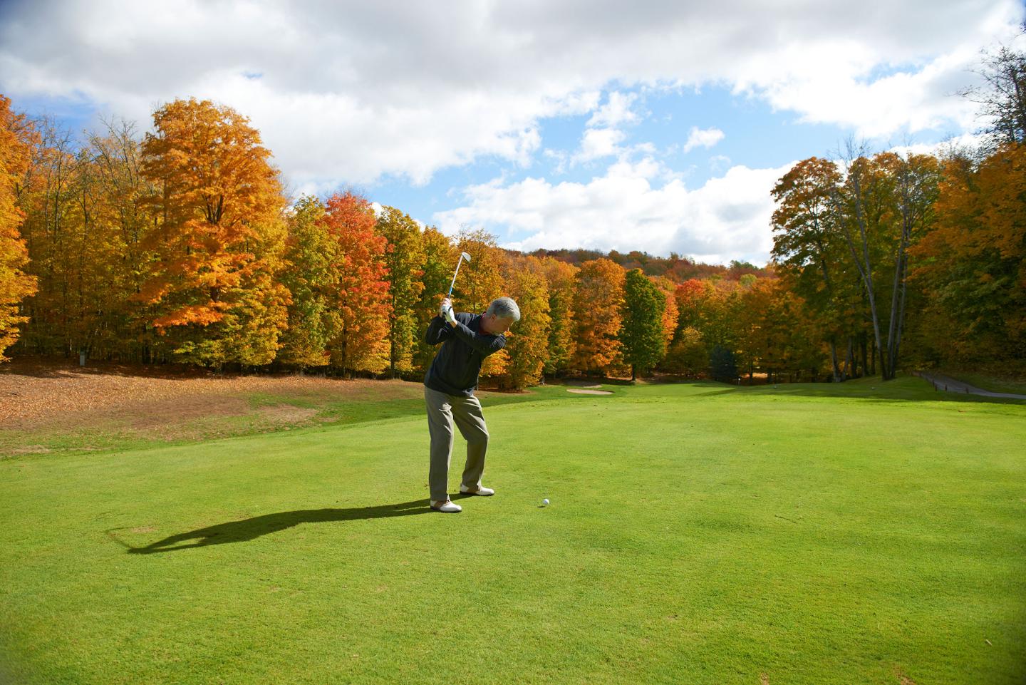 Golfer swinging on lush course with vibrant autumn trees.