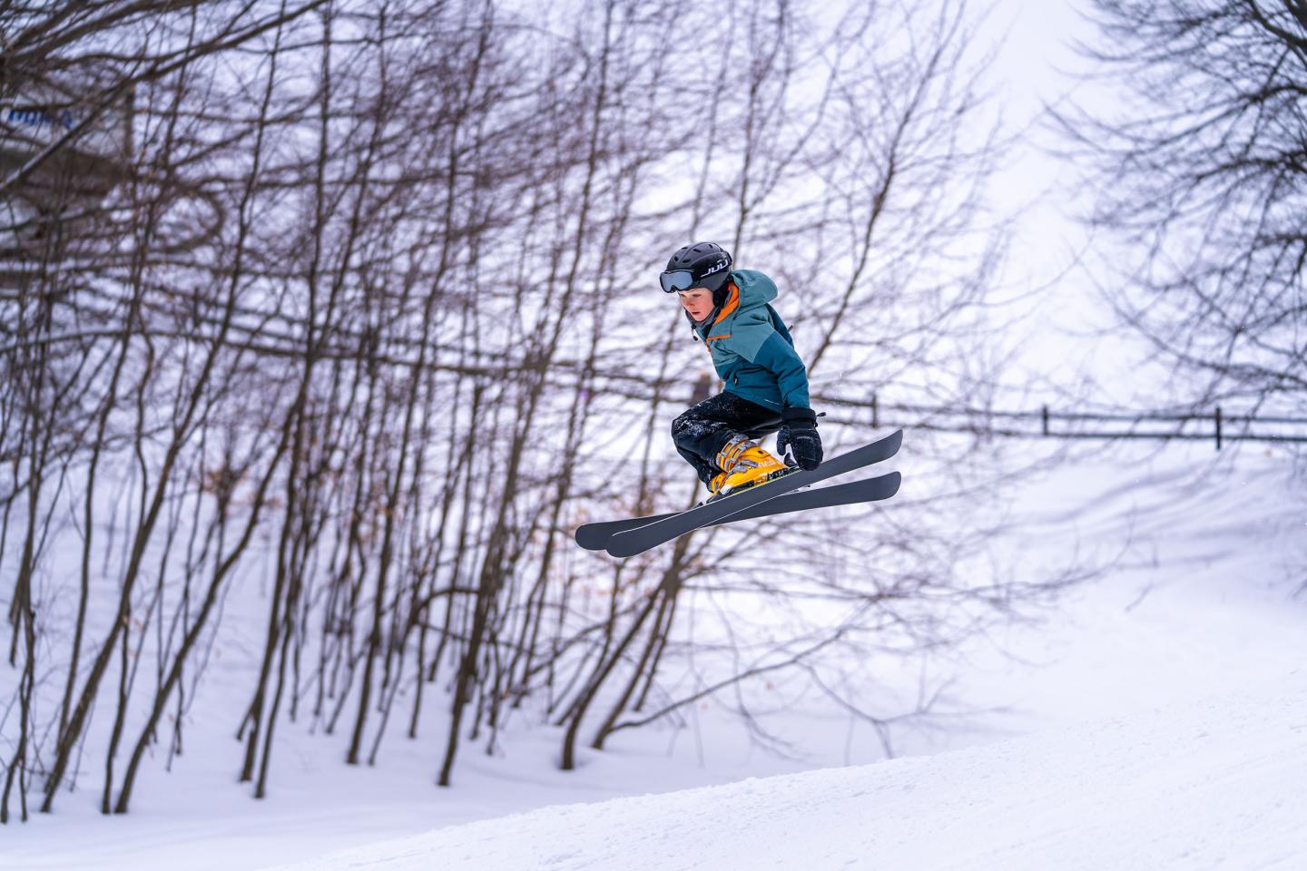 Skier jumping in snowy landscape, trees in background.