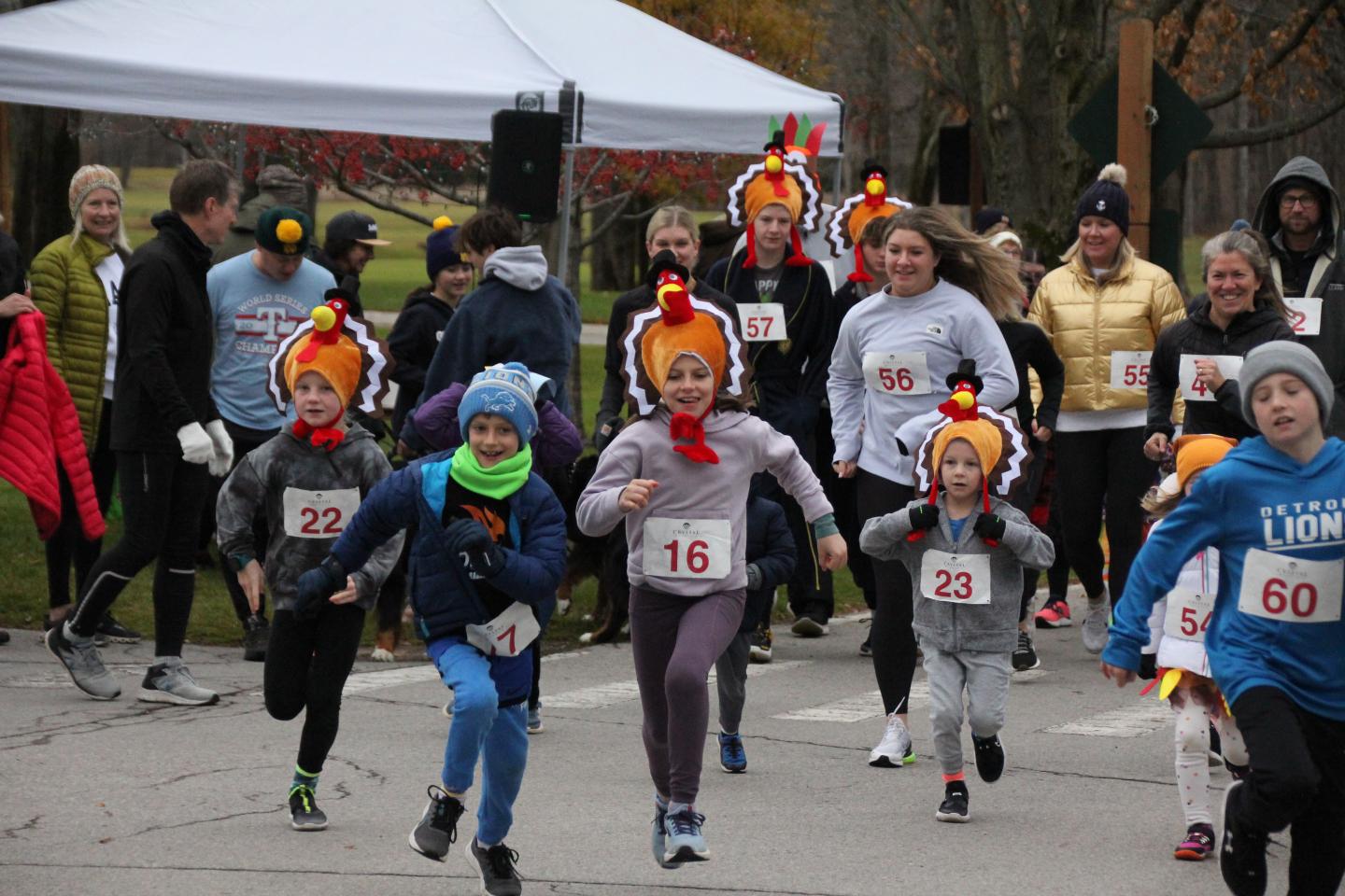 Runners in a race, wearing turkey hats and numbered bibs, outdoors.