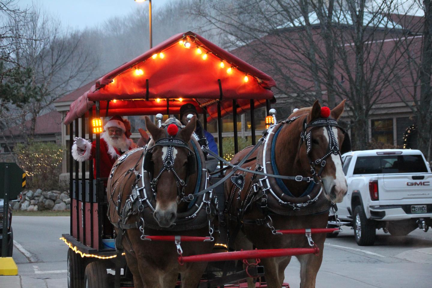 Horse-drawn carriage with Santa, lit by string lights, in a winter town setting.