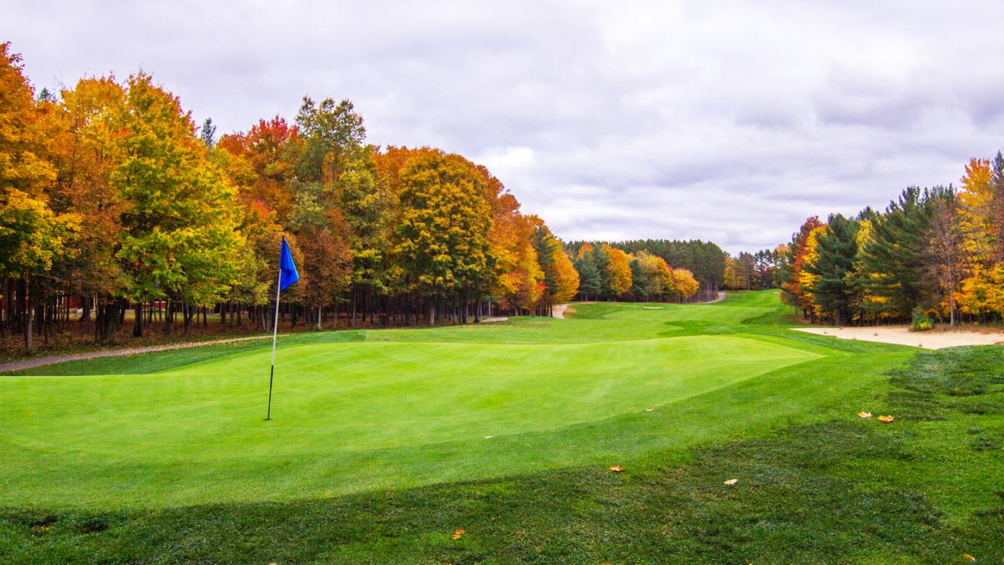 Golf course with autumn trees and cloudy sky.