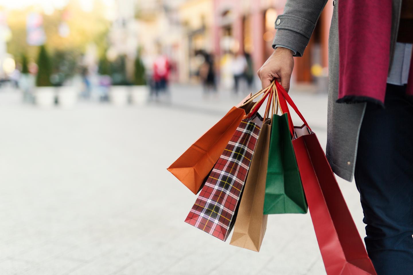 Hand holding multiple colorful shopping bags outdoors.