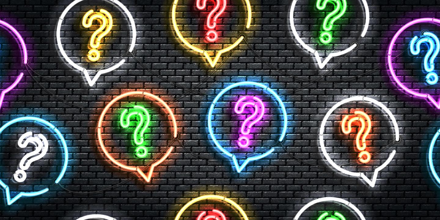 Neon question marks in colorful speech bubbles on a dark brick wall.