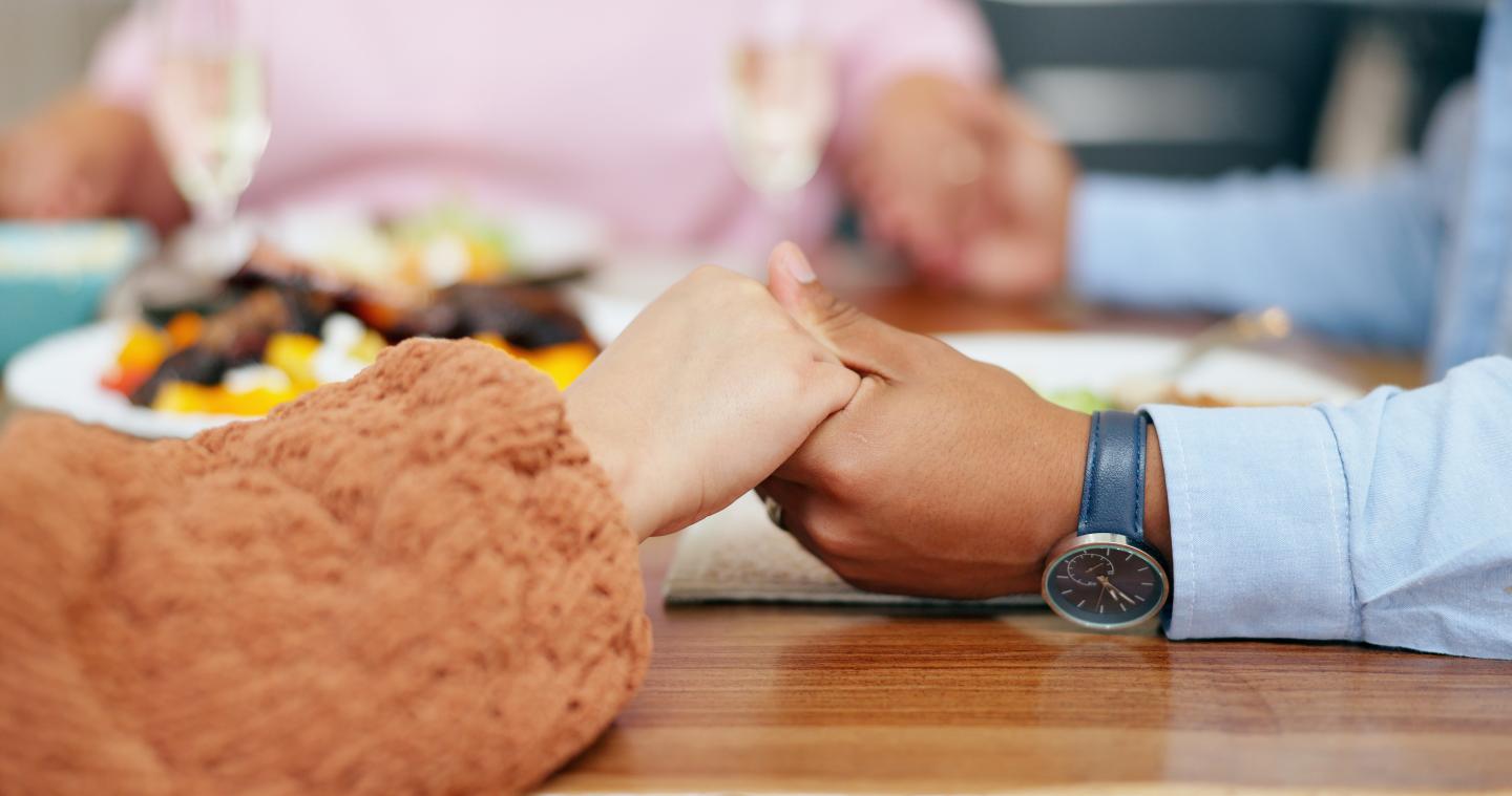 Hands holding across a table with dishes and champagne glasses.