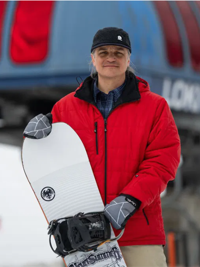 Person in red jacket holding snowboard, standing outside in winter.