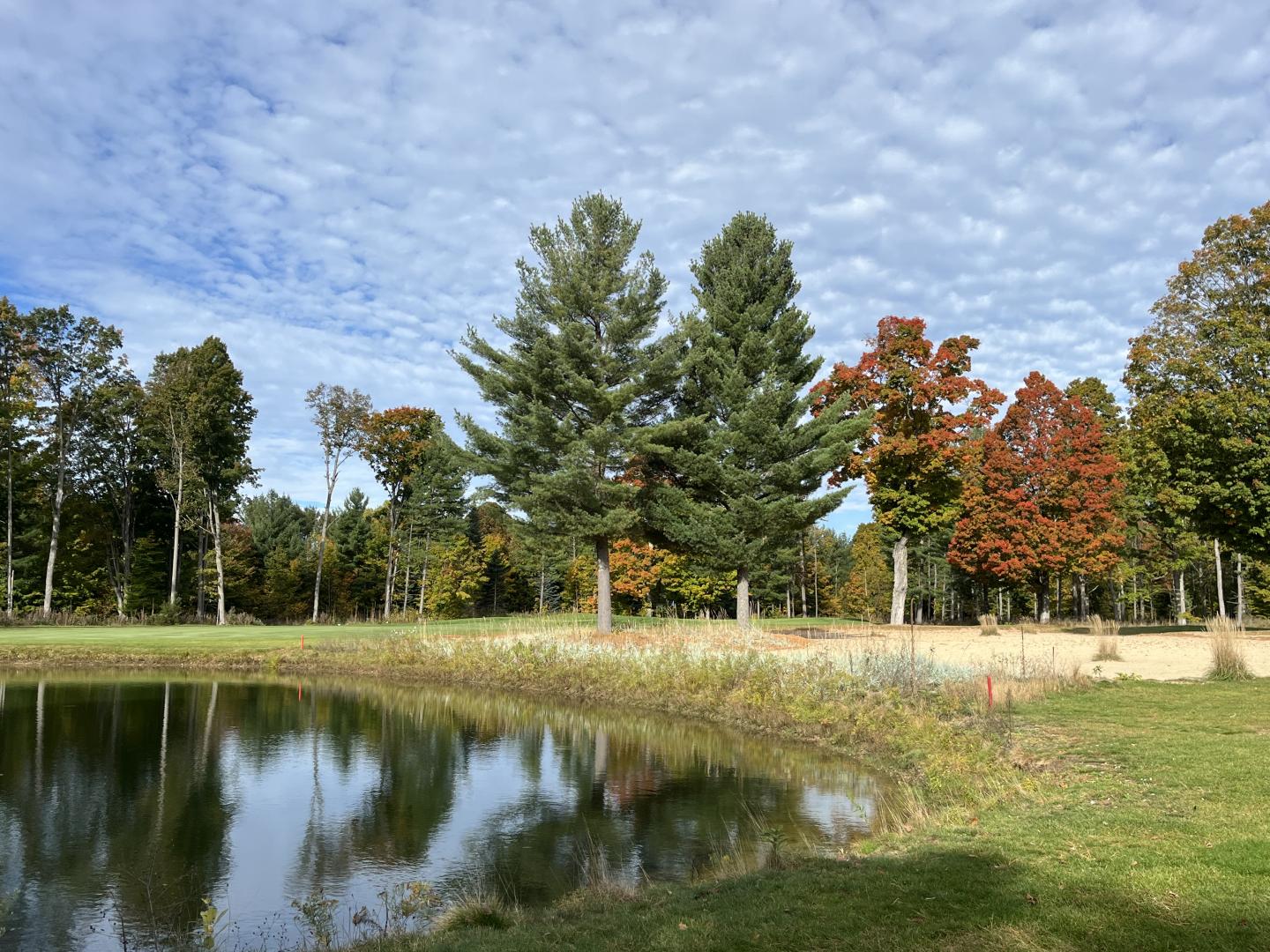 Trees on the Mountain ridge golf course with autumn foliage reflected in a pond under a cloudy sky.