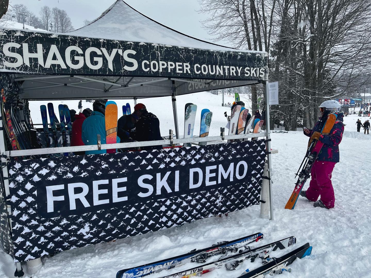 Ski demo tent on snowy day with people and colorful skis.