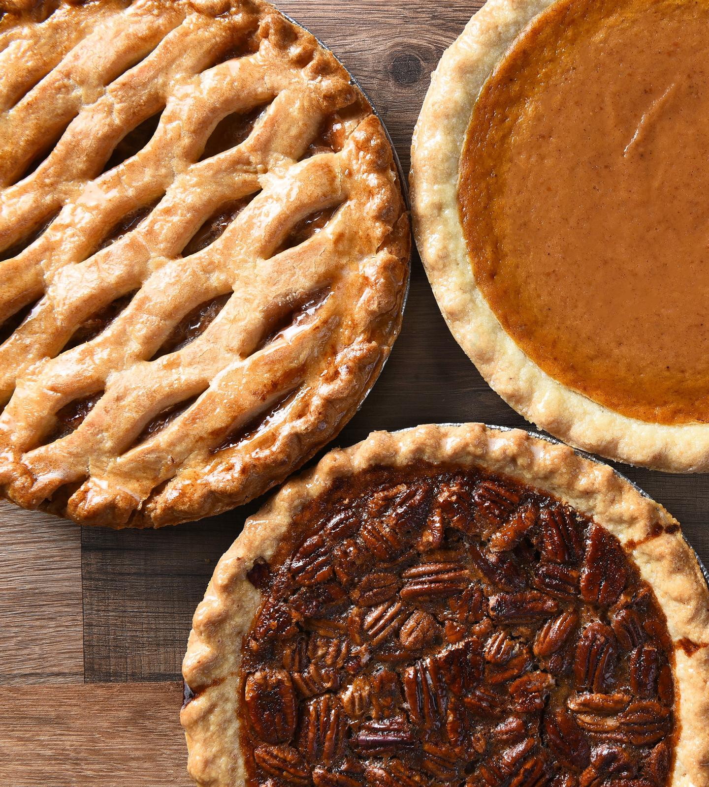Three pies on a wooden table: lattice apple, pumpkin, and pecan.