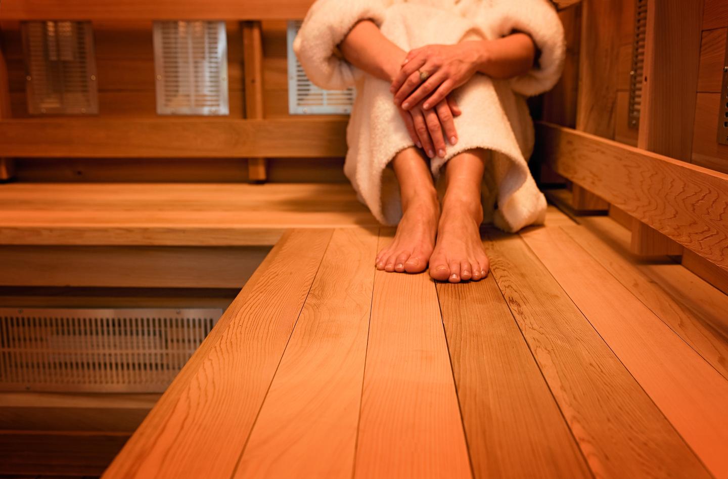Seated person in a sauna with a wooden interior.