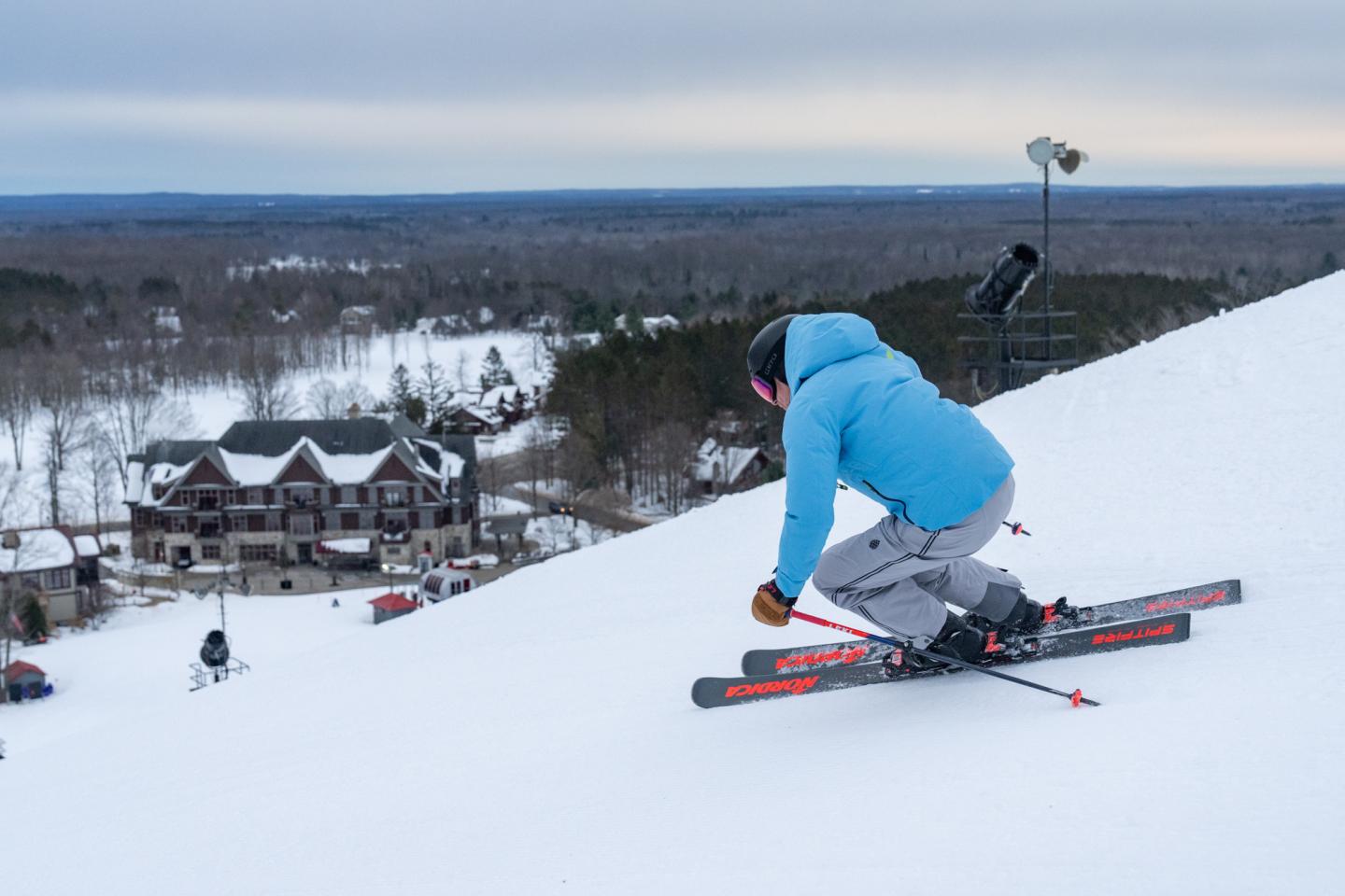 Skier in blue jacket descends snowy hill, Kinlochen and trees in background.