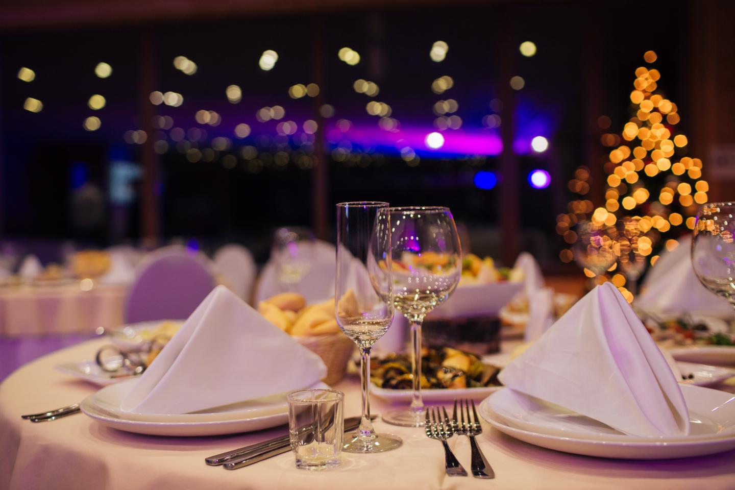 Elegant table setting, dimly lit with Christmas tree in the background.