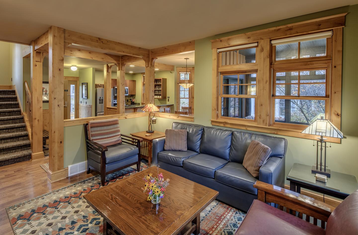 Cozy living room with blue sofa, armchairs, and wooden accents. Warm lighting and a rug.