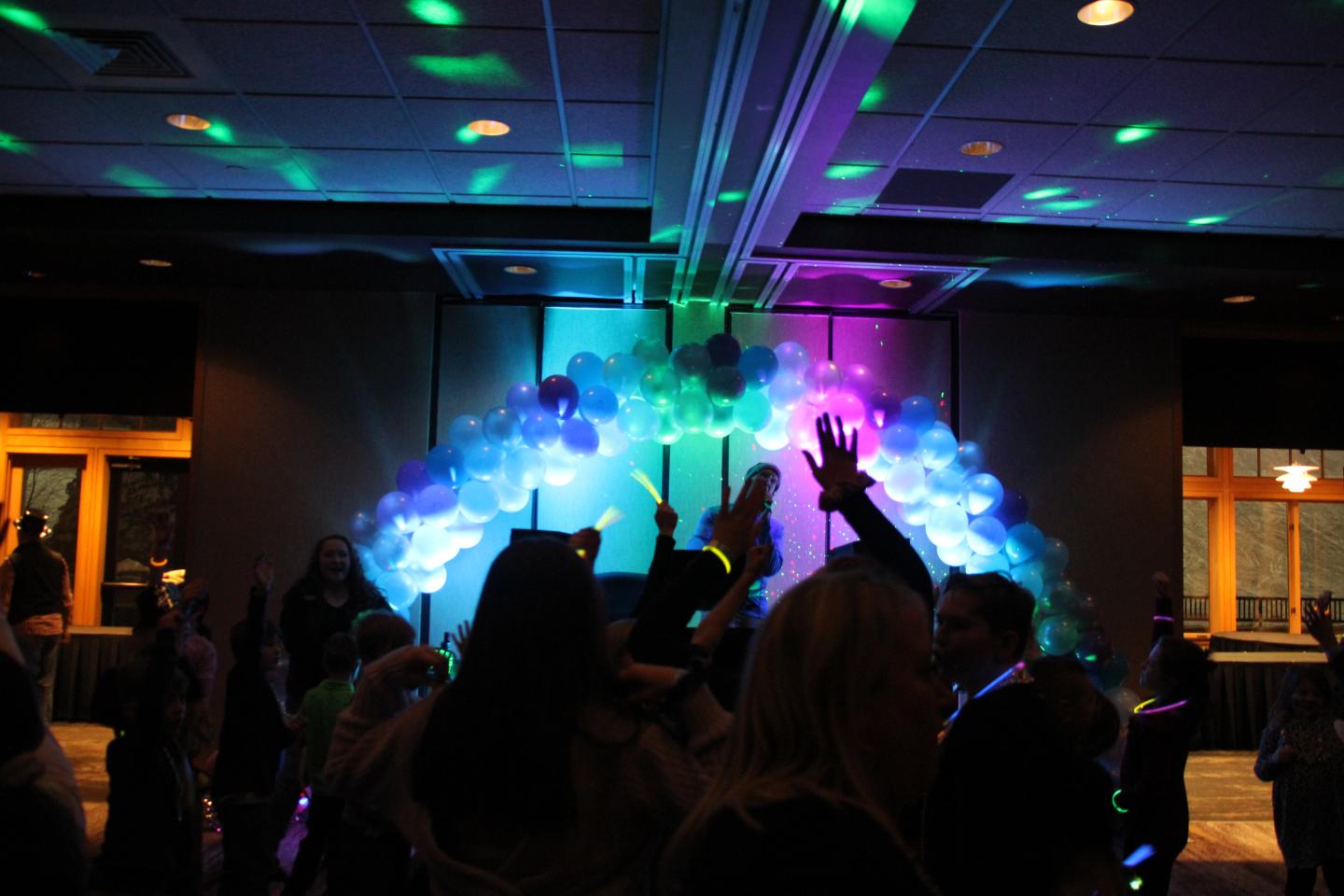 Dark room with colorful lights and people dancing, balloons on wall.