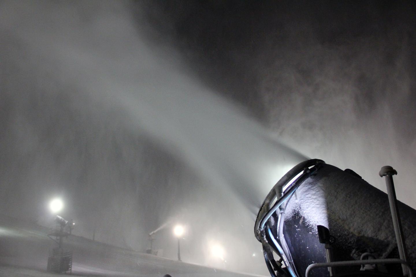 Snow machine blowing snow at night with lights illuminating the mist.