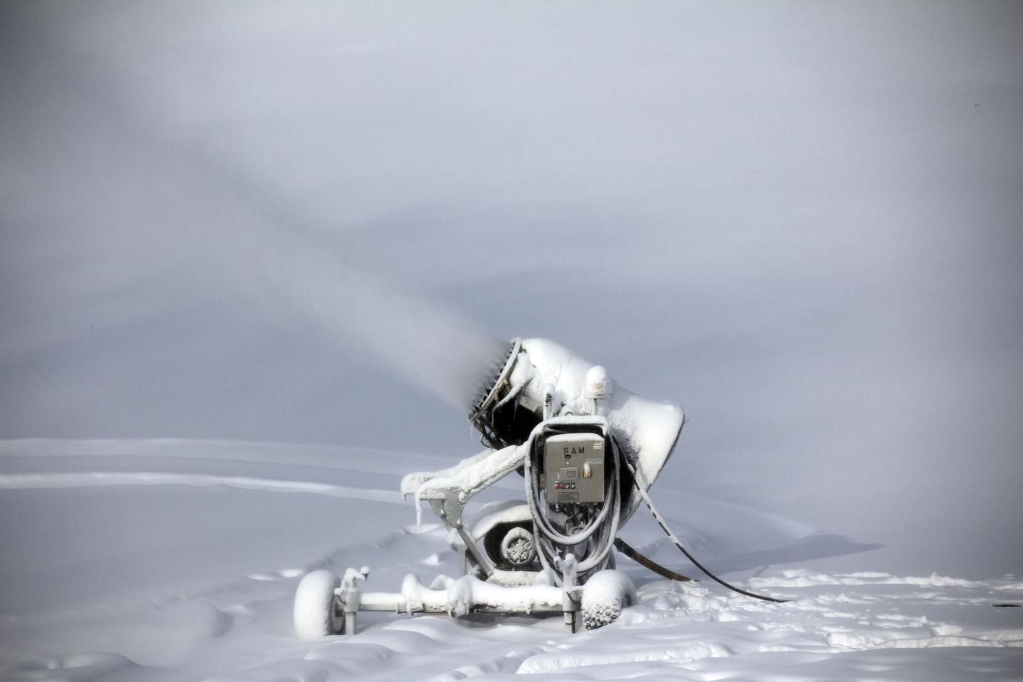 Snow-covered machine spraying snow on a snowy landscape.