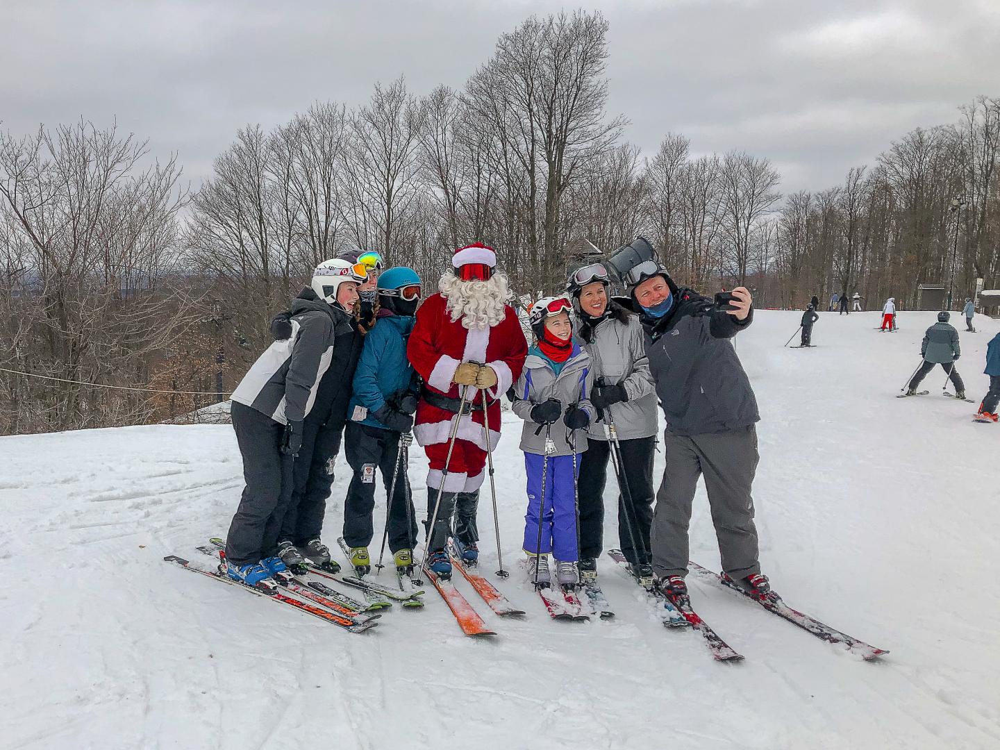 Skiers pose for a selfie with Santa on a snowy slope.