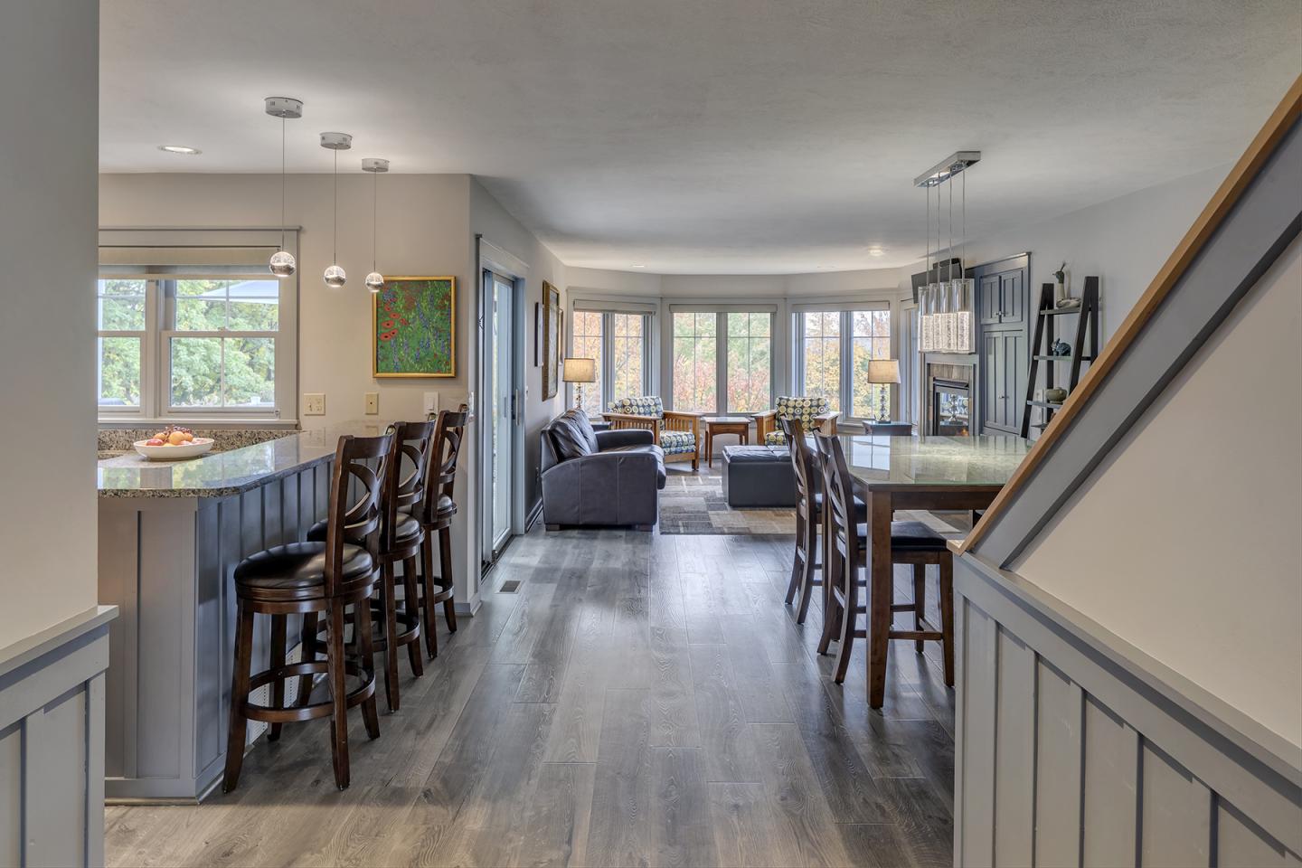 Modern living room with bar stools and gray sofas, large windows in background.