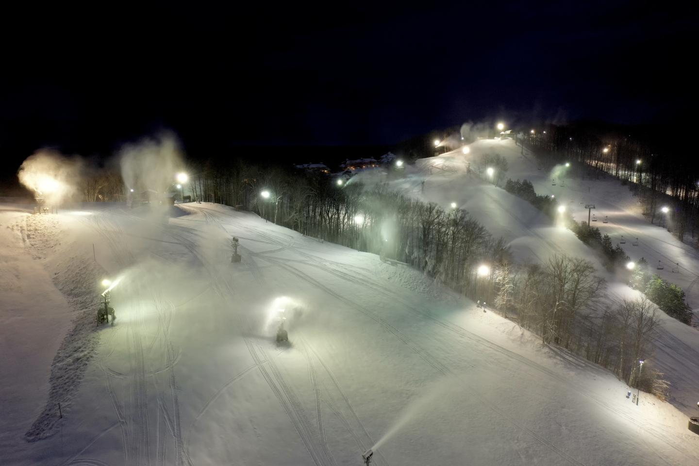 Snow-covered ski slope at night with bright lights and snow machines.