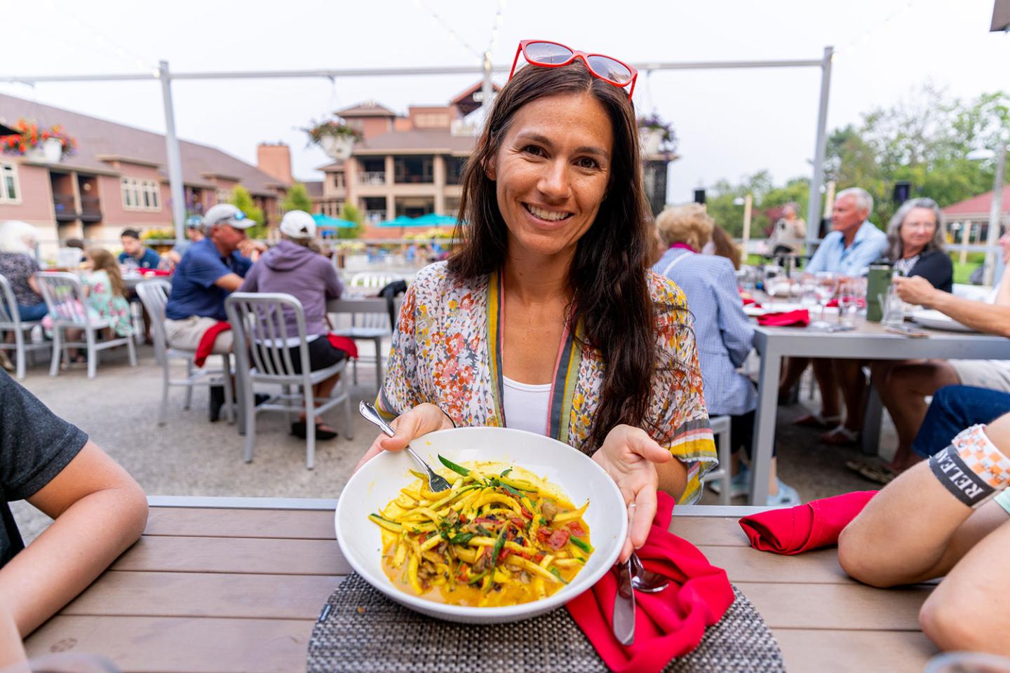 Woman smiling with a bowl of pasta at an outdoor restaurant.