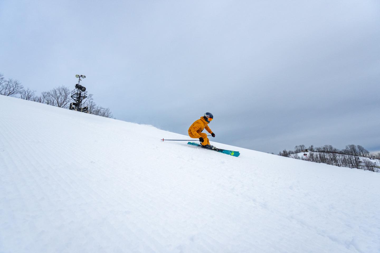 Skier in yellow suit descends a snowy slope under a cloudy sky.
