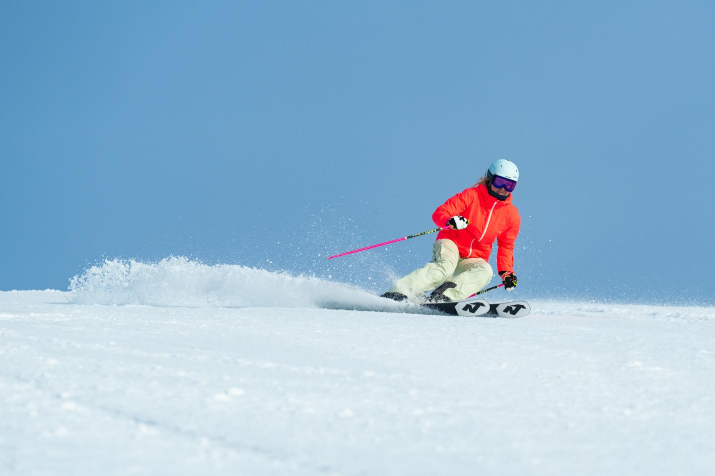 Skier in red jacket skiing downhill on a sunny day.