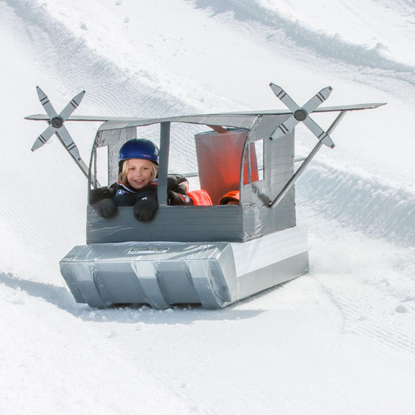 Child riding a snow sled shaped like an airplane on a snowy slope.