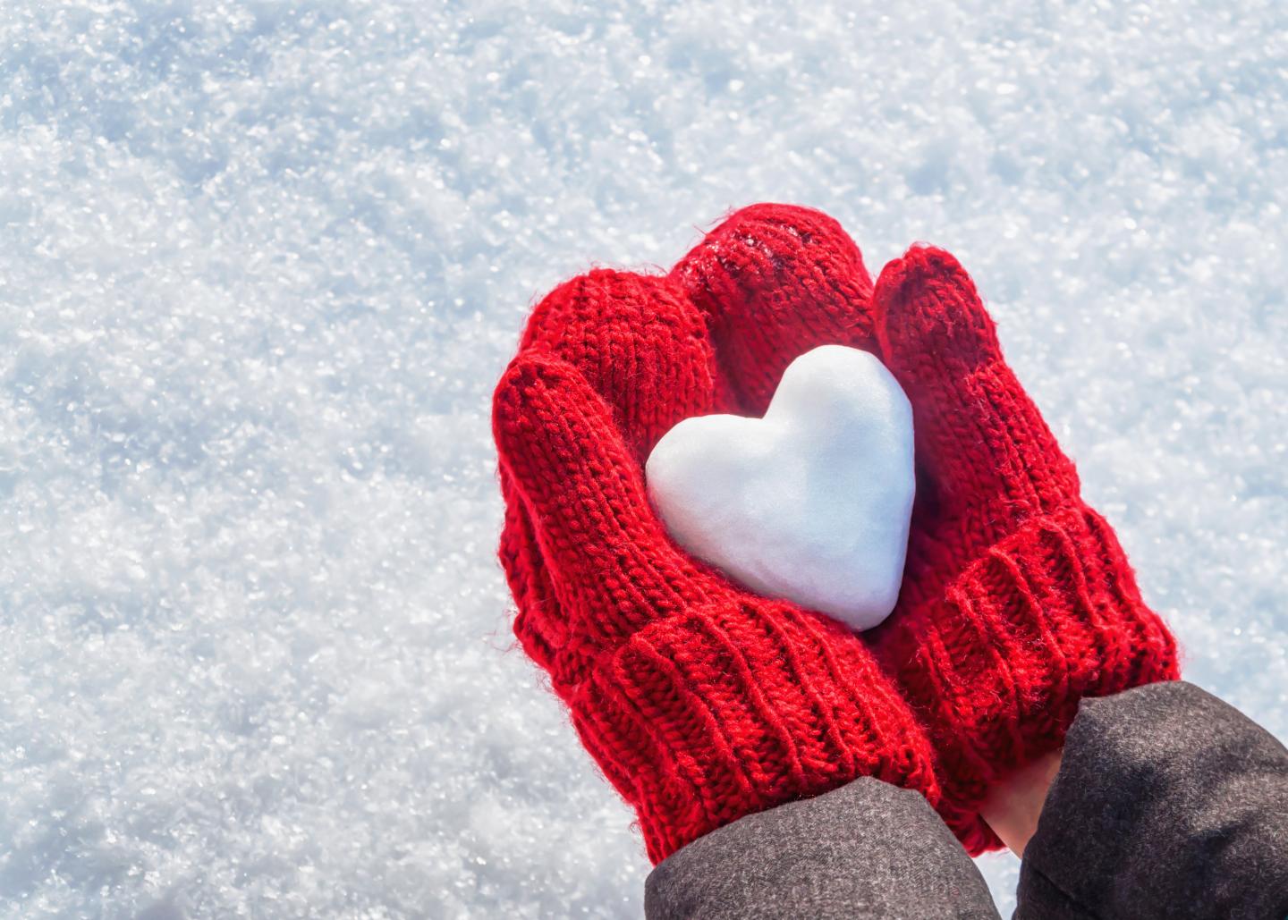 Red mittens holding a snow heart against a snowy background.
