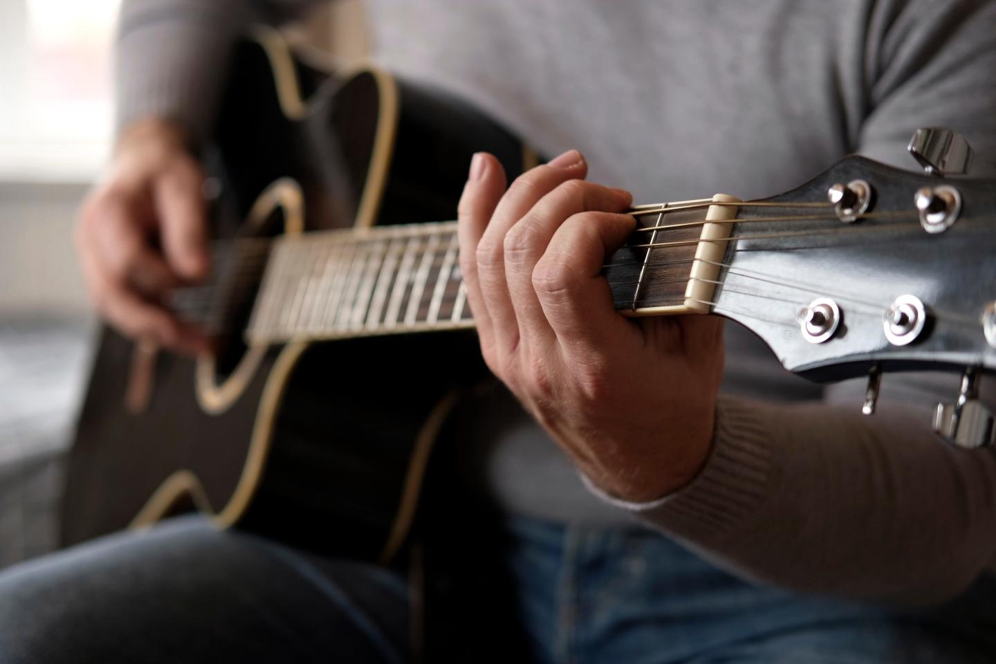 Man playing a black acoustic guitar indoors.