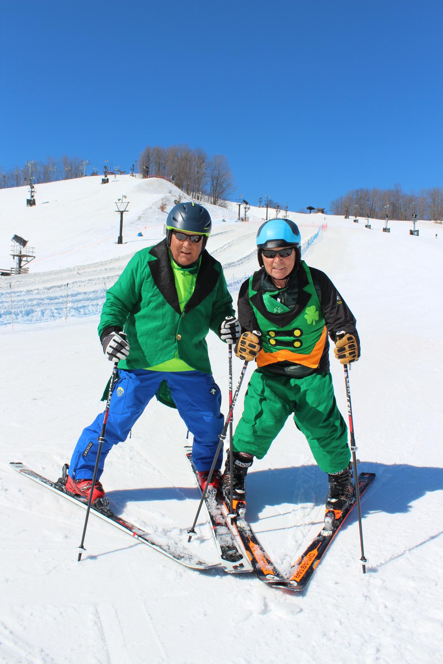 Two skiers in colorful outfits smiling on a sunny snow-covered slope.