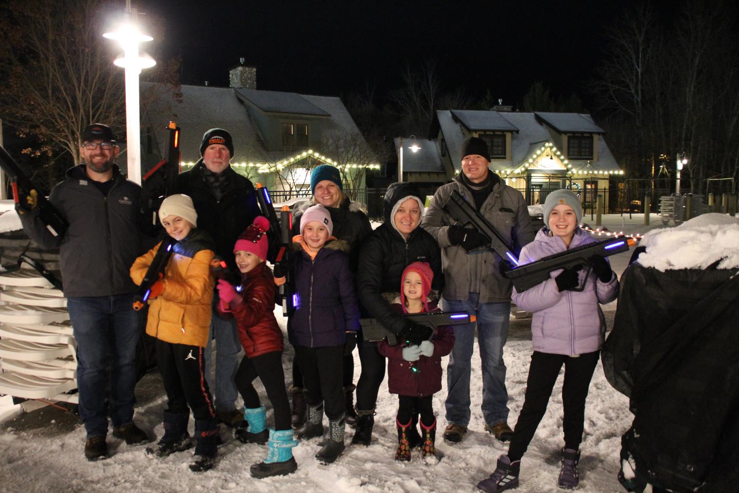 A group of people in winter clothing with lights, smiling at night playing Outdoor Laser Tag.