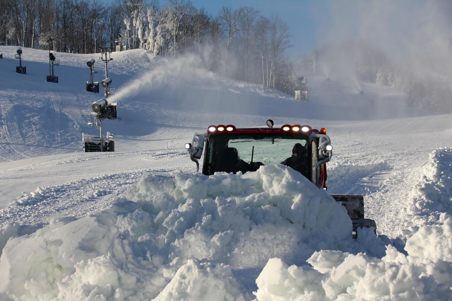 Red snowplow clearing snowy ski slope under blue sky.